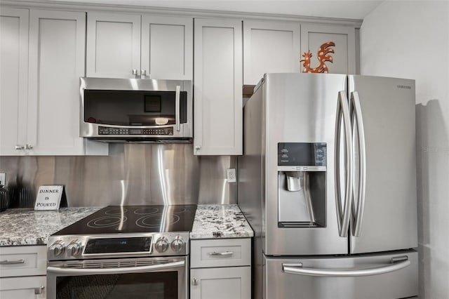 kitchen with gray cabinetry, decorative backsplash, light stone countertops, and appliances with stainless steel finishes