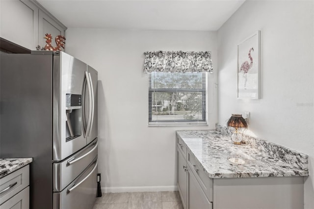 kitchen featuring gray cabinetry, light tile patterned floors, stainless steel fridge, and light stone countertops