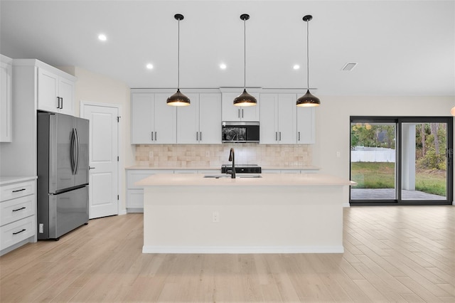 kitchen featuring white cabinetry, hanging light fixtures, appliances with stainless steel finishes, an island with sink, and decorative backsplash