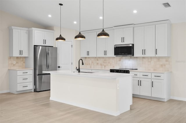 kitchen with pendant lighting, stainless steel refrigerator, white cabinetry, sink, and a center island with sink