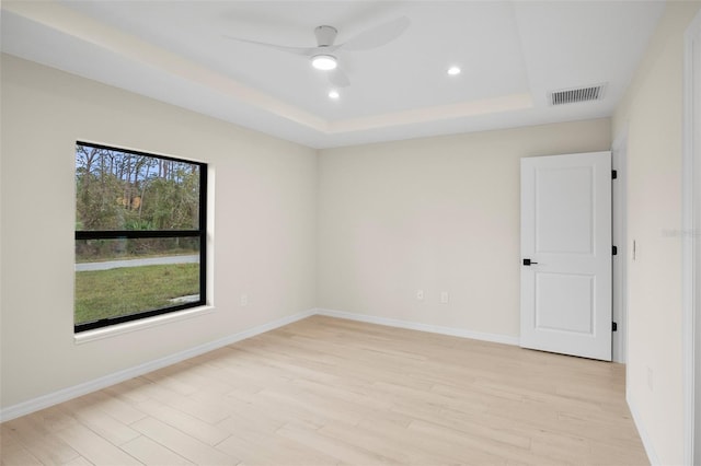 empty room featuring a tray ceiling, light hardwood / wood-style floors, and a healthy amount of sunlight