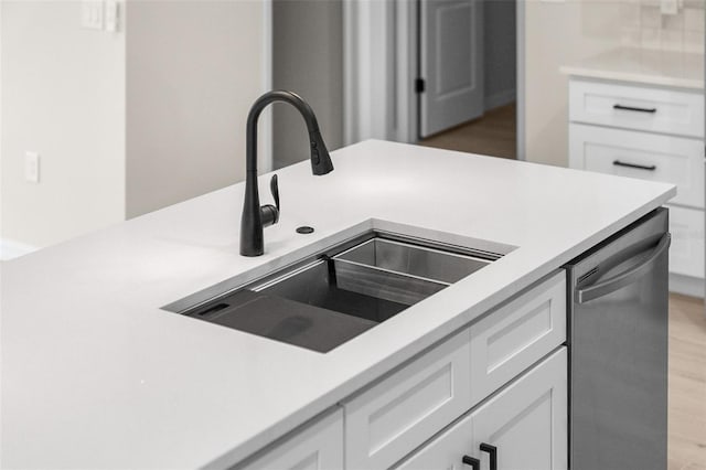 kitchen featuring white cabinetry, stainless steel dishwasher, sink, and light wood-type flooring