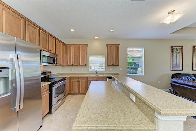 kitchen featuring sink, light tile patterned floors, appliances with stainless steel finishes, a textured ceiling, and a kitchen island