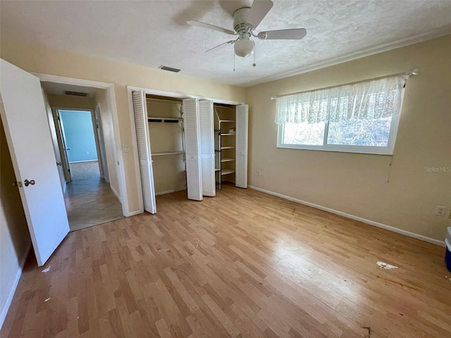 unfurnished bedroom featuring multiple closets, ceiling fan, a textured ceiling, and light wood-type flooring