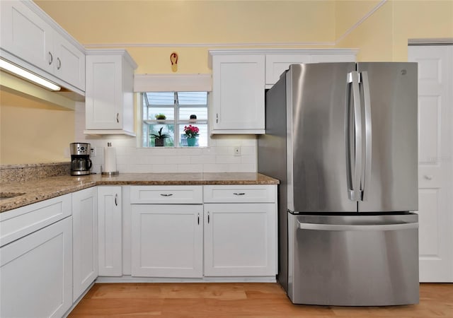 kitchen featuring stainless steel refrigerator, white cabinets, decorative backsplash, light stone countertops, and light hardwood / wood-style flooring