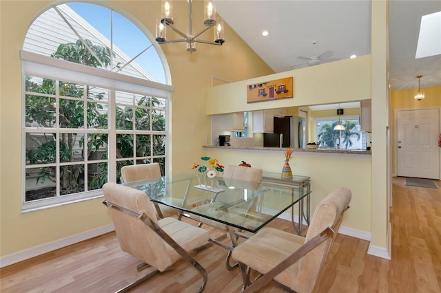 dining space featuring ceiling fan with notable chandelier, high vaulted ceiling, and light hardwood / wood-style floors