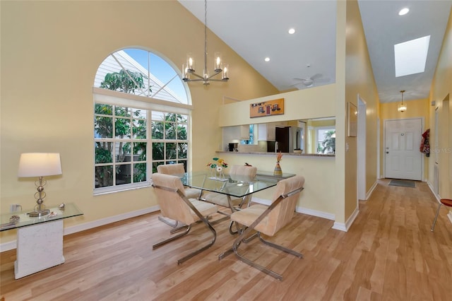 dining area featuring light wood-type flooring, ceiling fan with notable chandelier, and high vaulted ceiling