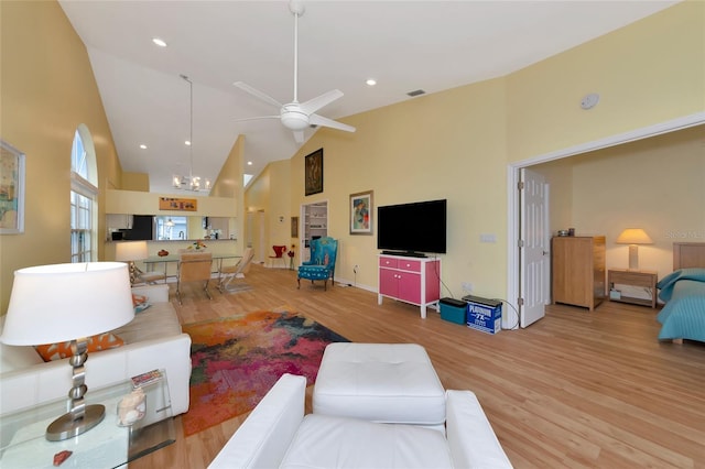 living room featuring ceiling fan with notable chandelier, wood-type flooring, and high vaulted ceiling