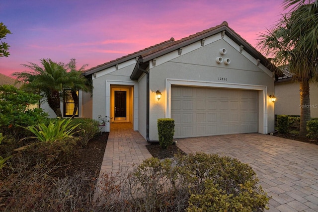 view of front facade featuring a garage, decorative driveway, and stucco siding