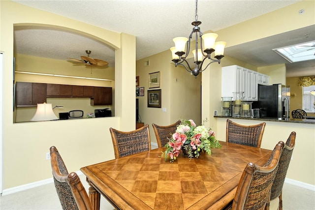 dining space with a skylight, ceiling fan with notable chandelier, and a textured ceiling