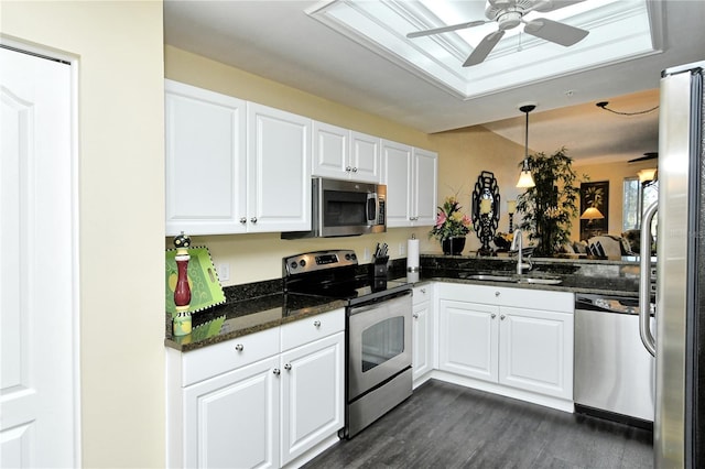 kitchen featuring appliances with stainless steel finishes, sink, dark stone countertops, white cabinets, and hanging light fixtures