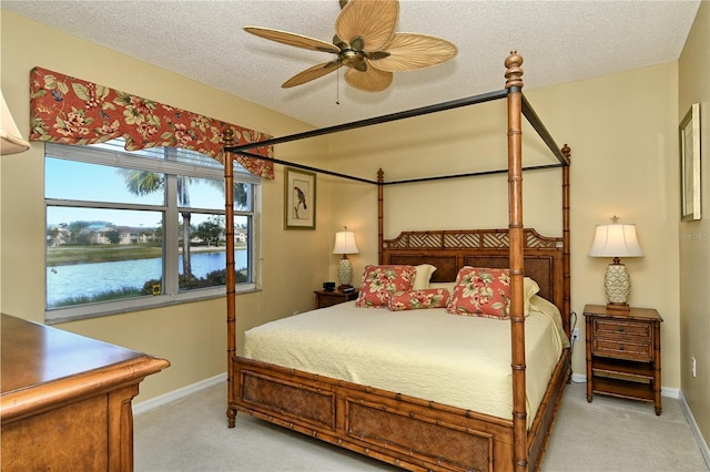 bedroom with a textured ceiling, light colored carpet, ceiling fan, and a water view