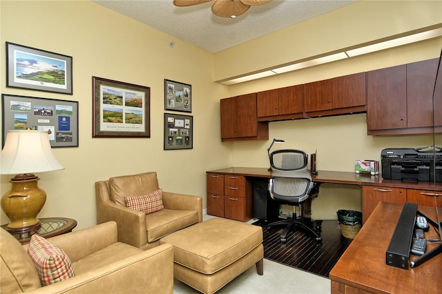 carpeted office space with ceiling fan, built in desk, and a textured ceiling