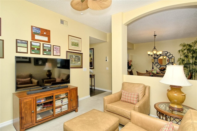 living room with carpet flooring, ceiling fan with notable chandelier, and a textured ceiling