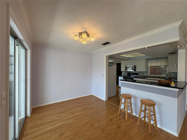 kitchen with light hardwood / wood-style flooring, a breakfast bar area, range, white cabinets, and kitchen peninsula