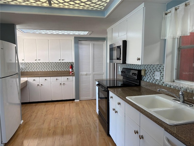 kitchen featuring sink, appliances with stainless steel finishes, white cabinetry, tasteful backsplash, and light hardwood / wood-style floors