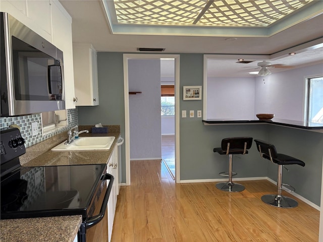 kitchen featuring sink, white cabinets, decorative backsplash, electric range, and light hardwood / wood-style flooring