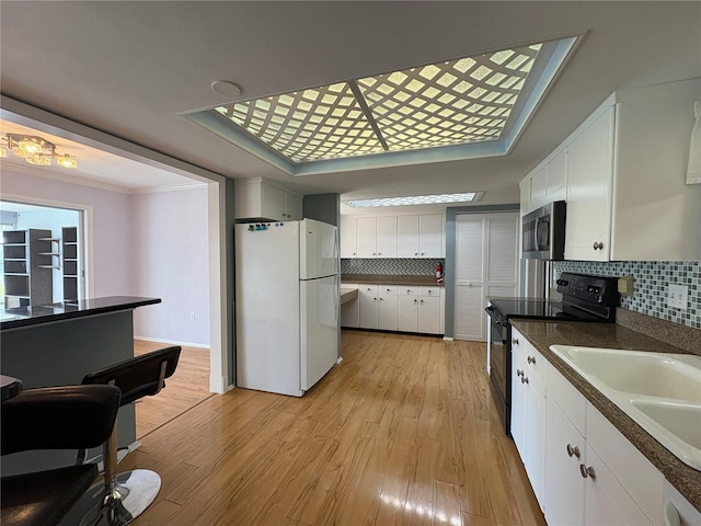 kitchen featuring white refrigerator, black range with electric stovetop, white cabinets, and light hardwood / wood-style flooring