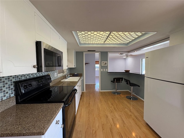 kitchen with sink, white cabinetry, light wood-type flooring, white refrigerator, and black / electric stove