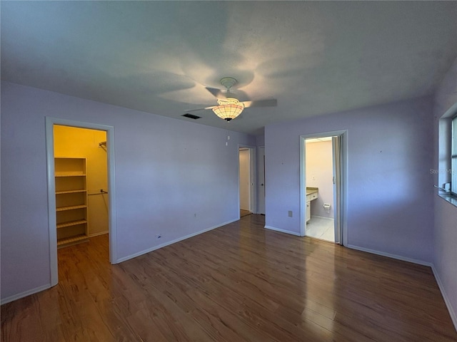 unfurnished bedroom featuring connected bathroom, a walk in closet, wood-type flooring, a closet, and ceiling fan