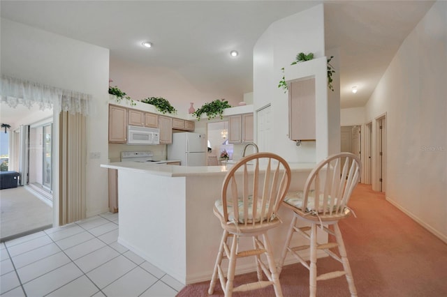 kitchen featuring a breakfast bar, light tile patterned floors, kitchen peninsula, light brown cabinets, and white appliances