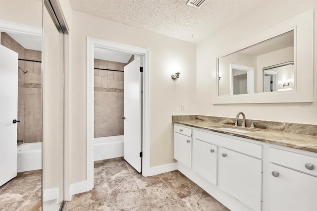 bathroom featuring vanity, a textured ceiling, and tiled shower / bath