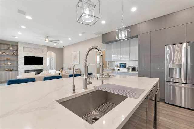 kitchen with sink, light stone counters, stainless steel fridge, gray cabinets, and pendant lighting