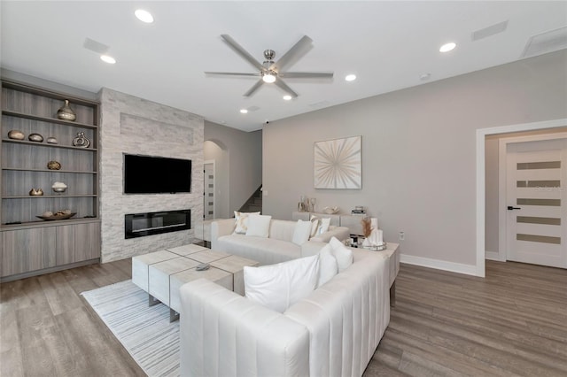 living room with built in shelves, light hardwood / wood-style flooring, a stone fireplace, and ceiling fan