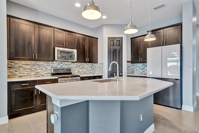 kitchen with sink, appliances with stainless steel finishes, hanging light fixtures, dark brown cabinets, and an island with sink