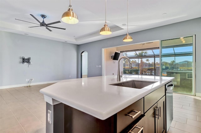 kitchen featuring a raised ceiling, sink, pendant lighting, and a kitchen island with sink