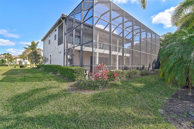 back of property featuring a balcony, glass enclosure, and a lawn