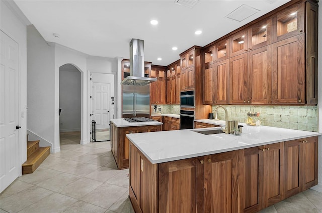 kitchen featuring tasteful backsplash, sink, built in refrigerator, island exhaust hood, and kitchen peninsula