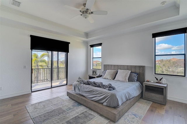 bedroom with hardwood / wood-style flooring, ceiling fan, access to exterior, a tray ceiling, and ornamental molding