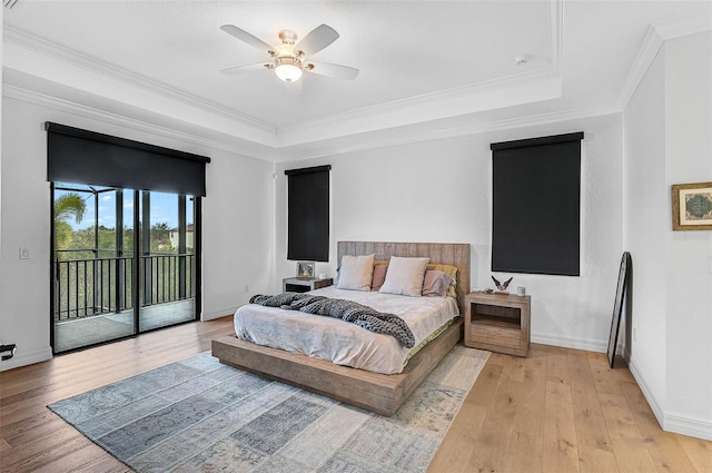 bedroom featuring access to exterior, a tray ceiling, light hardwood / wood-style flooring, and ornamental molding