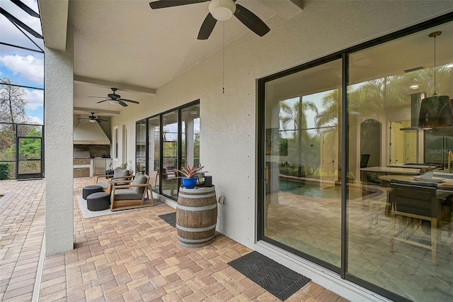 view of patio with ceiling fan, an outdoor kitchen, and glass enclosure