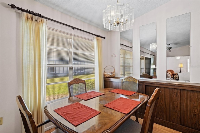 dining area with wood-type flooring, ceiling fan with notable chandelier, and a textured ceiling