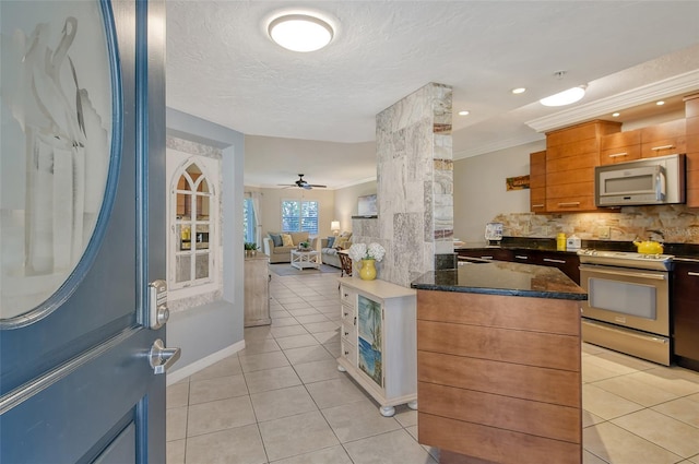 kitchen featuring appliances with stainless steel finishes, tasteful backsplash, dark stone counters, light tile patterned floors, and crown molding