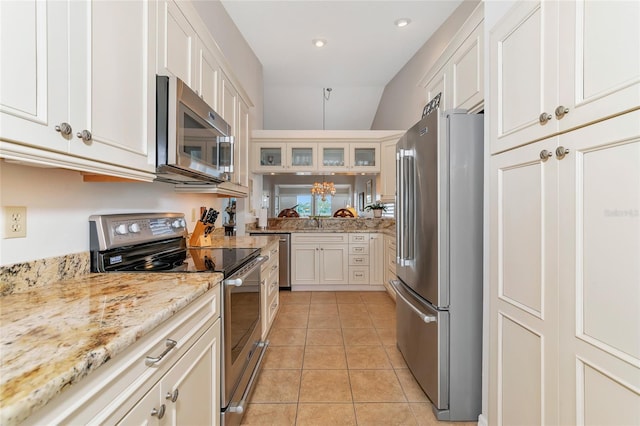 kitchen featuring white cabinetry, light stone counters, vaulted ceiling, light tile patterned floors, and appliances with stainless steel finishes