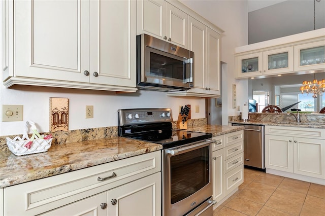 kitchen with sink, appliances with stainless steel finishes, light stone counters, light tile patterned flooring, and a chandelier