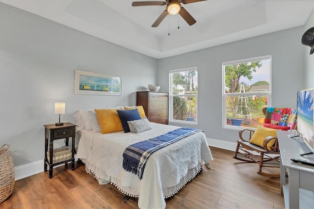 bedroom with hardwood / wood-style floors, a raised ceiling, and ceiling fan