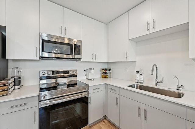 kitchen with stainless steel appliances, sink, white cabinets, and light hardwood / wood-style floors