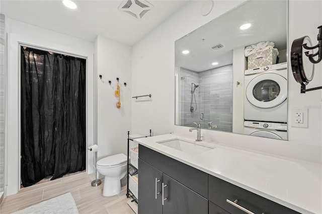 bathroom with stacked washer / drying machine, toilet, vanity, and a tile shower