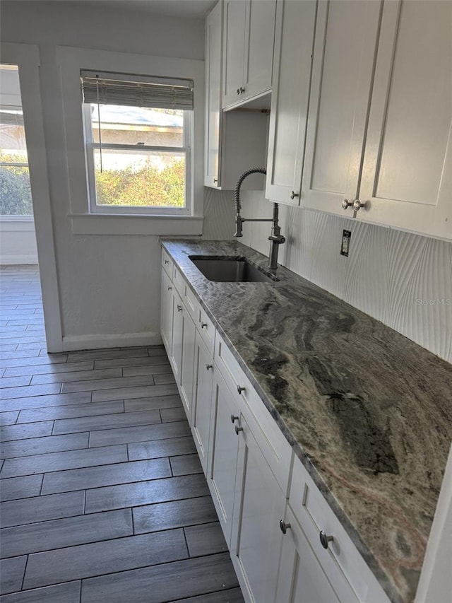 kitchen with tasteful backsplash, white cabinets, sink, and dark stone countertops