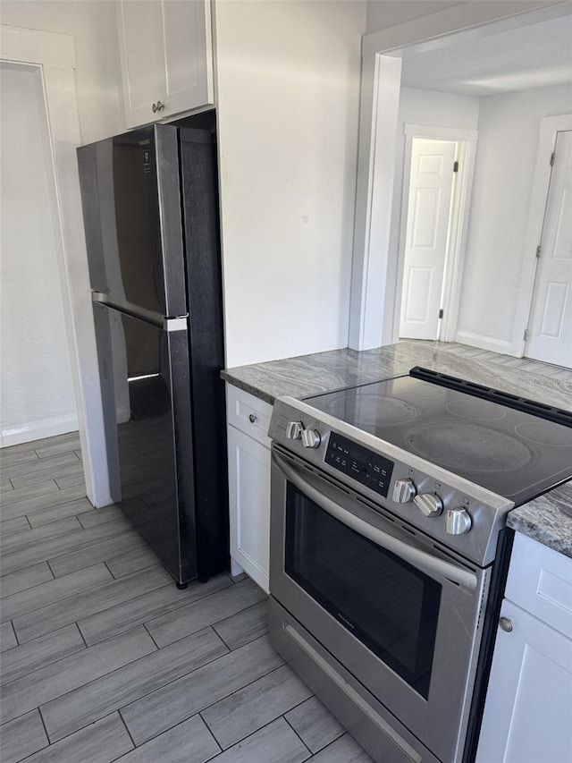 kitchen featuring white cabinetry, black fridge, dark stone counters, and stainless steel electric range