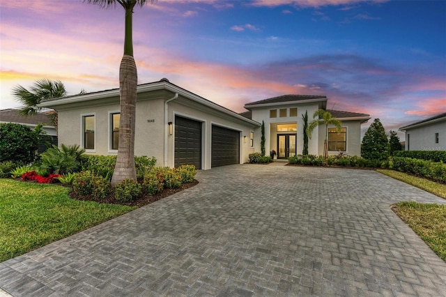 view of front facade featuring stucco siding, french doors, an attached garage, and decorative driveway