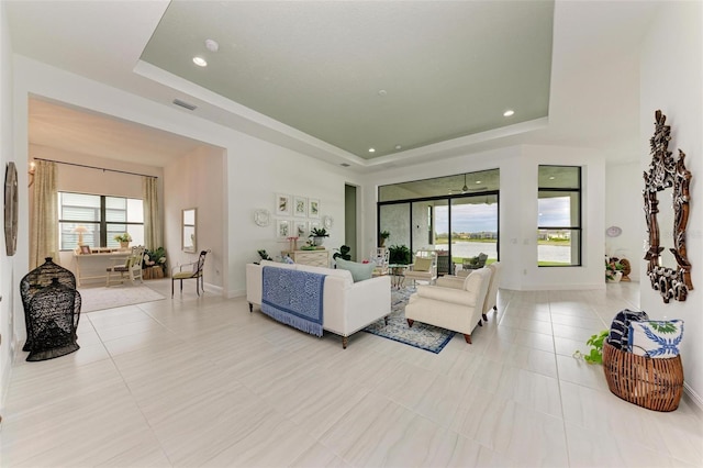 living area with a wealth of natural light, a tray ceiling, and light tile patterned flooring