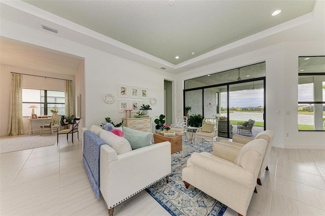 tiled living room with a water view, a raised ceiling, and a wealth of natural light