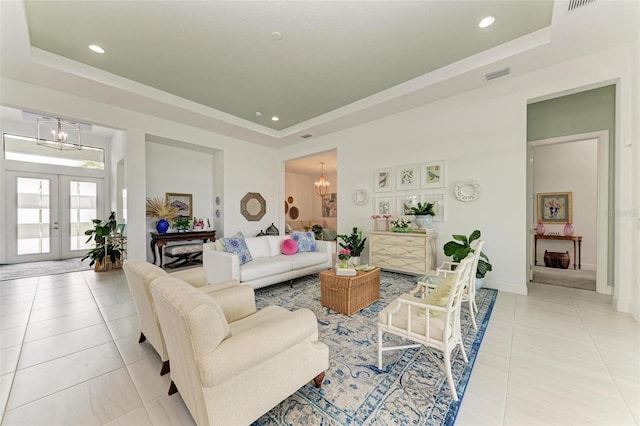 living room with a chandelier, light tile patterned floors, and a tray ceiling