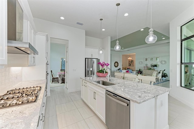 kitchen featuring wall chimney range hood, a center island with sink, white cabinets, stainless steel appliances, and a sink