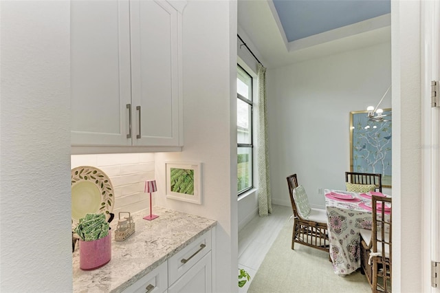 interior space featuring light stone counters, backsplash, white cabinetry, baseboards, and a chandelier